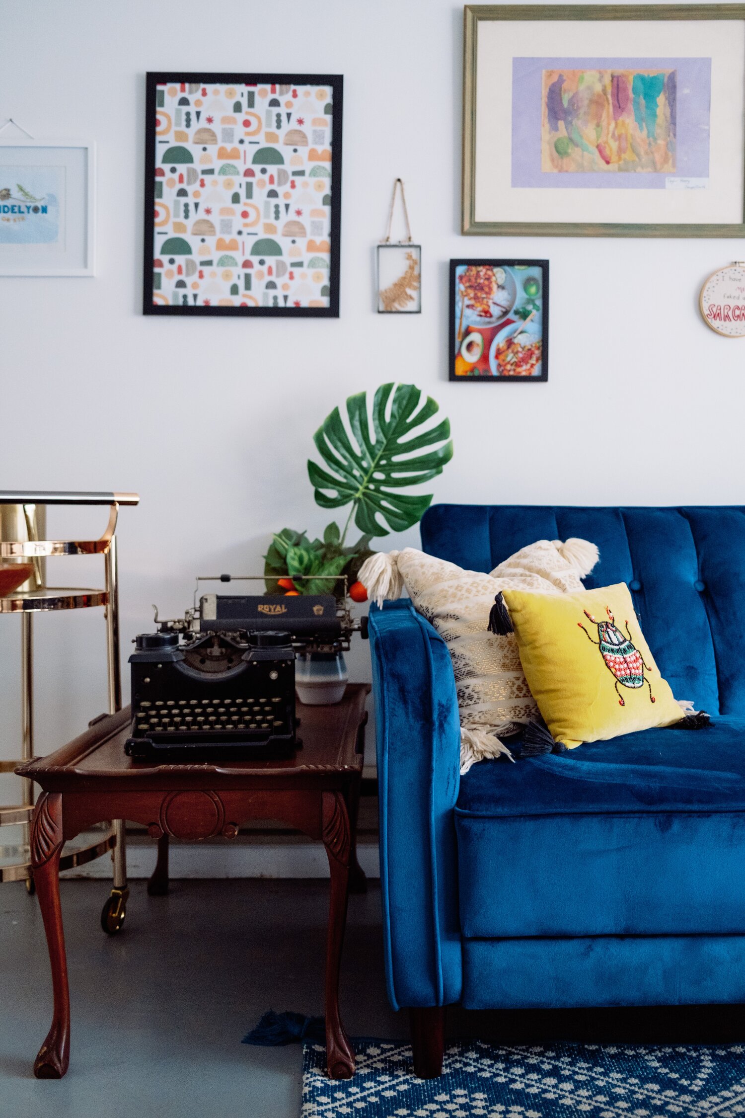 A blue velvet sofa in a living room adorned with wall pictures.