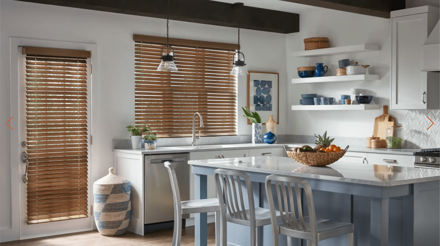 Bright kitchen with white cabinets, a blue-gray island, and wooden blinds over the sink on both windows.