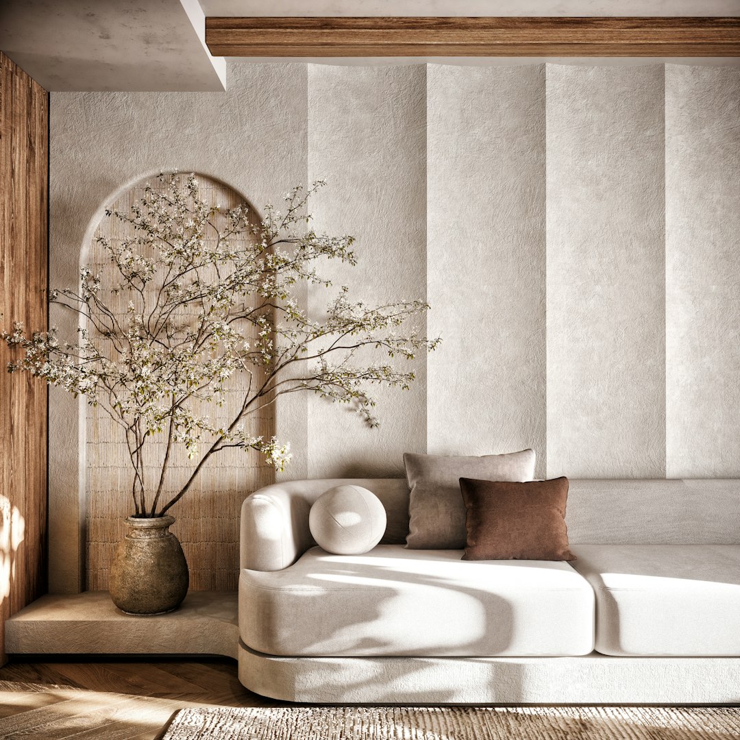 Beige sectional sofa with brown and beige cushions beside a tall vase with flowering branches in a sunlit modern living room.