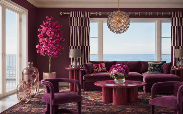 Luxurious purple living room with velvet sofa, pink accents, and an ocean view through large windows above the sea.
